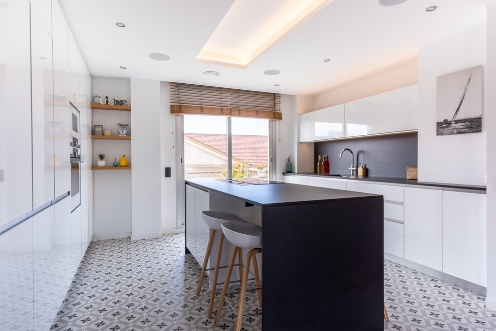 Inspiration for a large scandi open plan kitchen in Barcelona with a submerged sink, flat-panel cabinets, white cabinets, engineered stone countertops, black splashback, integrated appliances, cement flooring, an island, multi-coloured floors and black worktops.