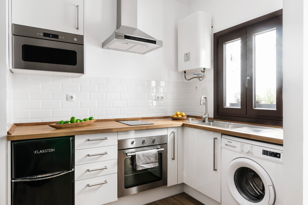 Idéer för ett litet modernt beige l-kök, med en undermonterad diskho, släta luckor, vita skåp, träbänkskiva, vitt stänkskydd, stänkskydd i tunnelbanekakel, rostfria vitvaror och brunt golv