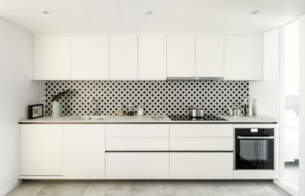 Diseño de cocina lineal mediterránea con armarios con paneles lisos, puertas de armario blancas, salpicadero negro, electrodomésticos negros y encimeras blancas