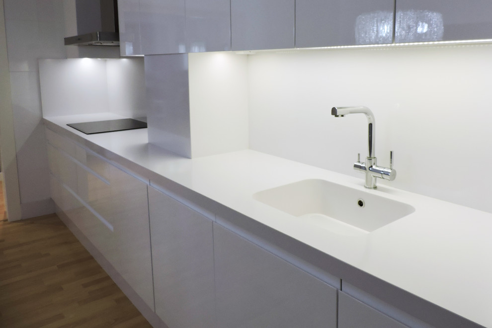 Inspiration for a modern enclosed kitchen in Dublin with an integrated sink, flat-panel cabinets, white cabinets, white splashback, integrated appliances and light hardwood flooring.