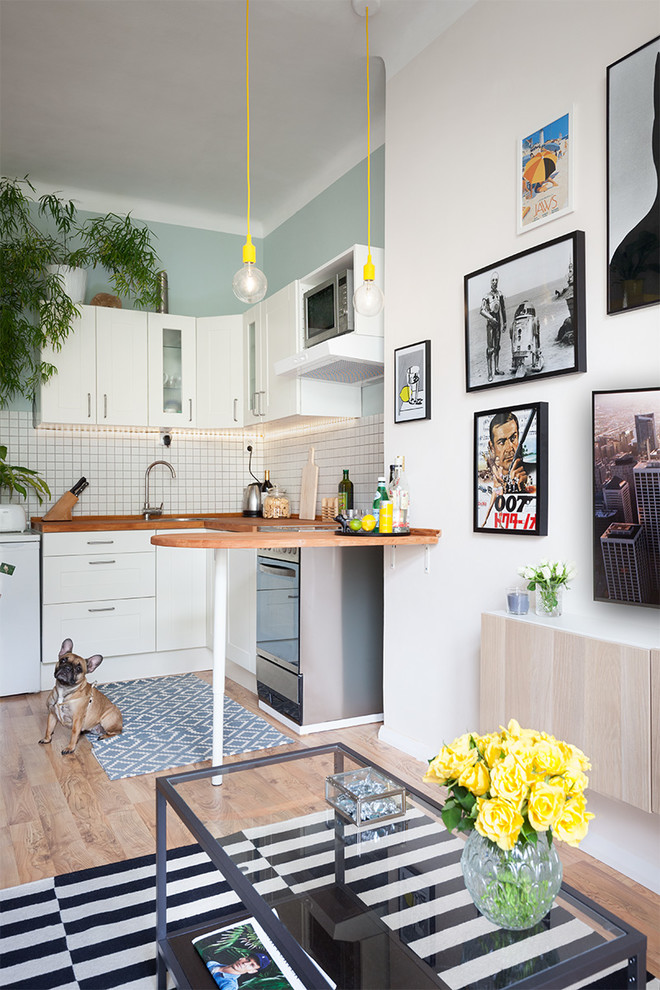 Foto de cocinas en L actual pequeña abierta con fregadero de un seno, armarios con rebordes decorativos, puertas de armario blancas, encimera de madera, salpicadero blanco, salpicadero con mosaicos de azulejos, electrodomésticos de acero inoxidable, suelo de madera clara y península