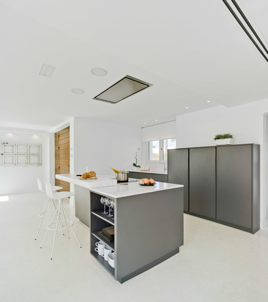 Cette photo montre une cuisine tendance de taille moyenne avec un placard à porte plane, îlot, un plan de travail blanc, des portes de placard grises et un sol beige.