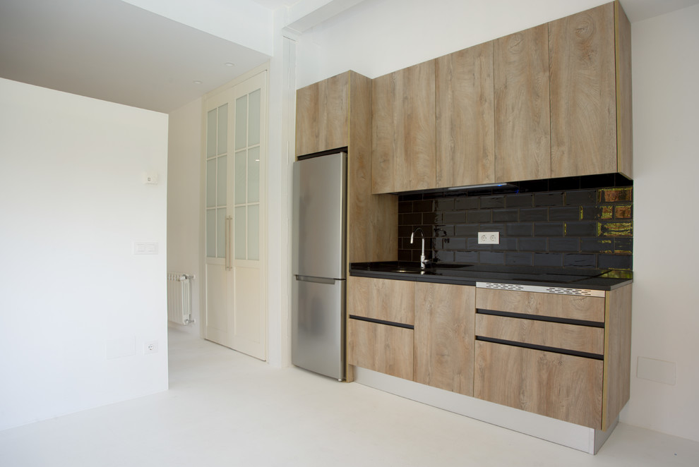 Photo of a small urban single-wall open plan kitchen in Madrid with a submerged sink, raised-panel cabinets, light wood cabinets, engineered stone countertops, black splashback, ceramic splashback, stainless steel appliances, plywood flooring, white floors and black worktops.