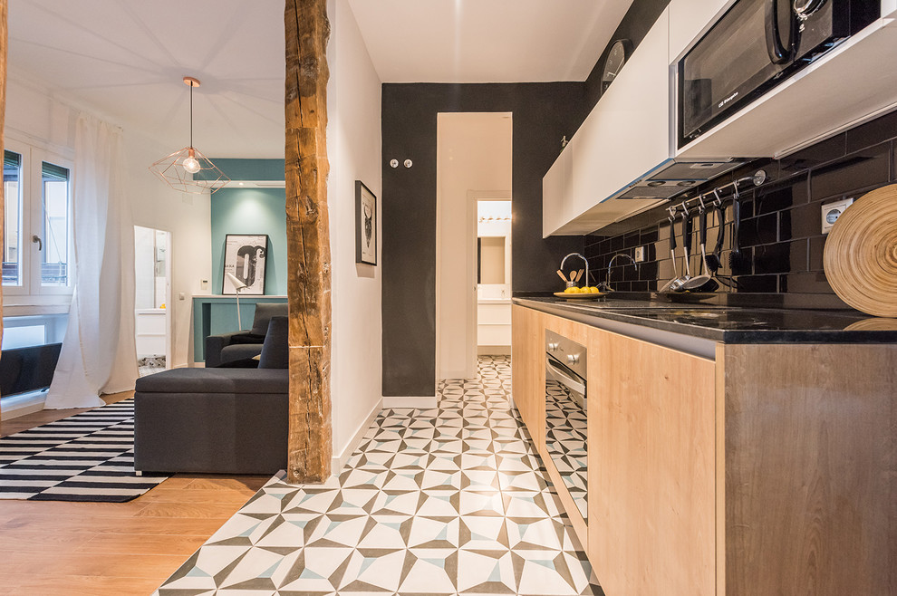 Foto på ett litet funkis linjärt kök med öppen planlösning, med släta luckor, skåp i ljust trä, svart stänkskydd, stänkskydd i tunnelbanekakel, marmorbänkskiva, rostfria vitvaror och klinkergolv i keramik