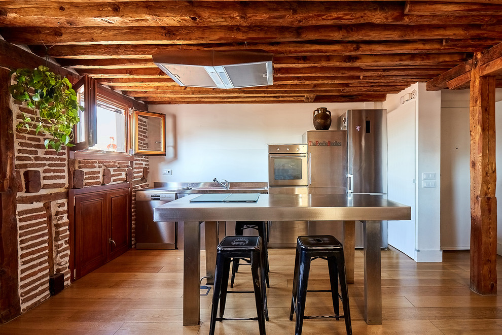Rustik inredning av ett litet grå linjärt grått kök och matrum, med en enkel diskho, skåp i rostfritt stål, bänkskiva i rostfritt stål, rostfria vitvaror, mellanmörkt trägolv, en köksö, brunt golv, släta luckor och brunt stänkskydd