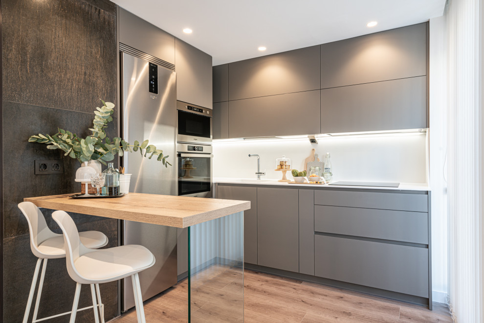 Design ideas for a medium sized contemporary l-shaped kitchen in Other with an integrated sink, flat-panel cabinets, grey cabinets, white splashback, stainless steel appliances, a breakfast bar, beige floors and white worktops.