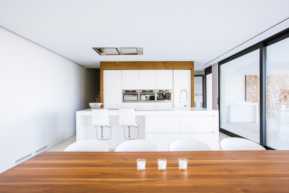 Foto de cocina lineal moderna grande abierta con armarios con paneles lisos, puertas de armario blancas, electrodomésticos de acero inoxidable y una isla