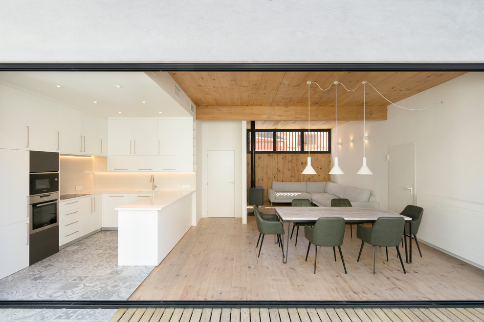 Идея дизайна: п-образная кухня-гостиная в современном стиле с плоскими фасадами, белыми фасадами, техникой из нержавеющей стали, полуостровом, серым полом и белой столешницей