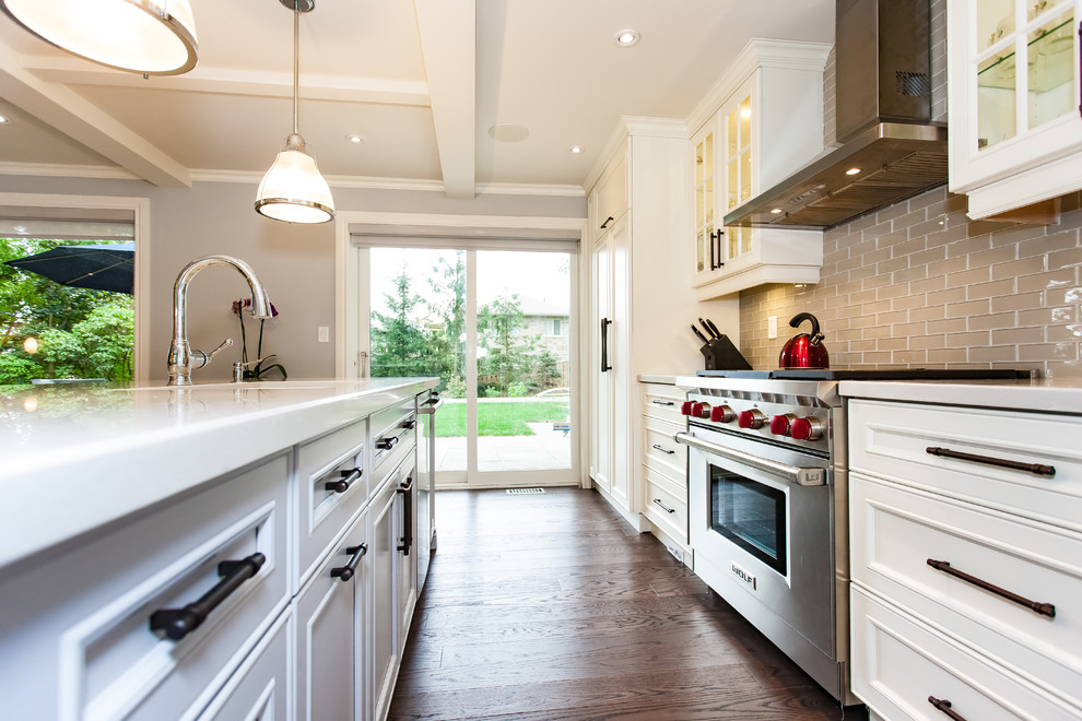 Example of a large transitional galley medium tone wood floor and brown floor kitchen design in Toronto with an undermount sink, recessed-panel cabinets, white cabinets, brown backsplash, glass tile backsplash, stainless steel appliances and an island