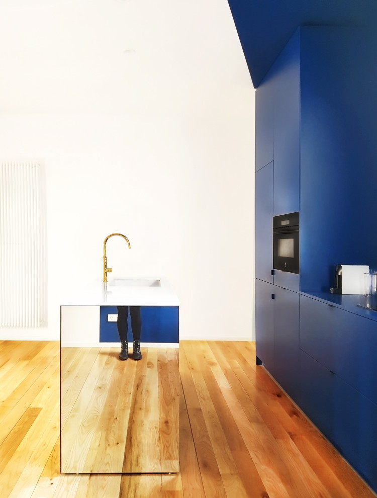 Offene, Einzeilige, Mittelgroße Moderne Küche mit Landhausspüle, Schrankfronten im Shaker-Stil, blauen Schränken, Quarzwerkstein-Arbeitsplatte, Küchenrückwand in Blau, braunem Holzboden, Kücheninsel und weißer Arbeitsplatte in Madrid