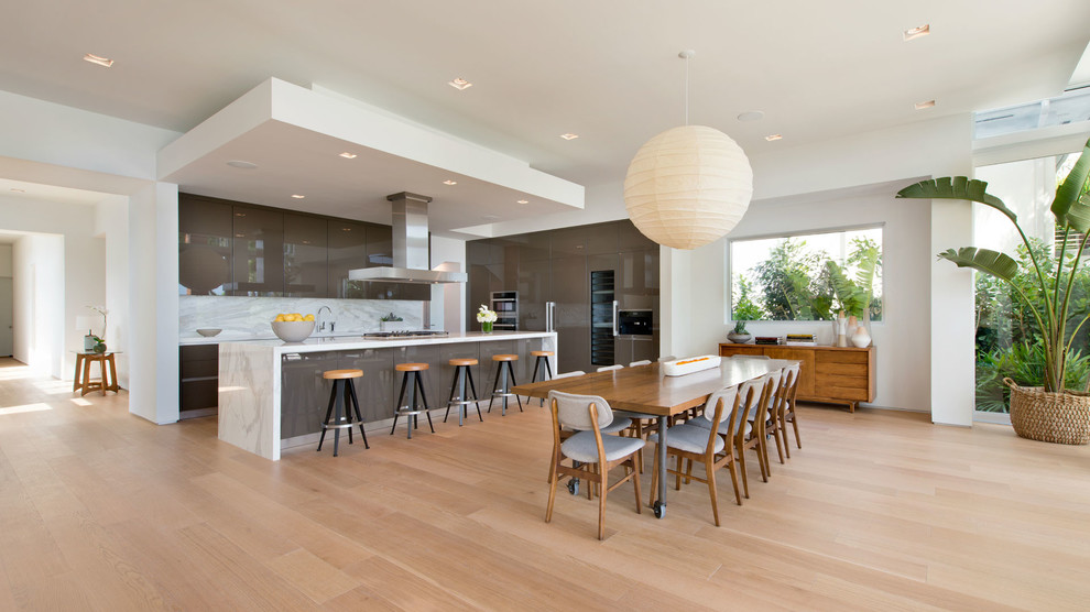 Offene Moderne Küche in L-Form mit flächenbündigen Schrankfronten, Küchenrückwand in Weiß, hellem Holzboden, weißer Arbeitsplatte, grauen Schränken, Kücheninsel und beigem Boden