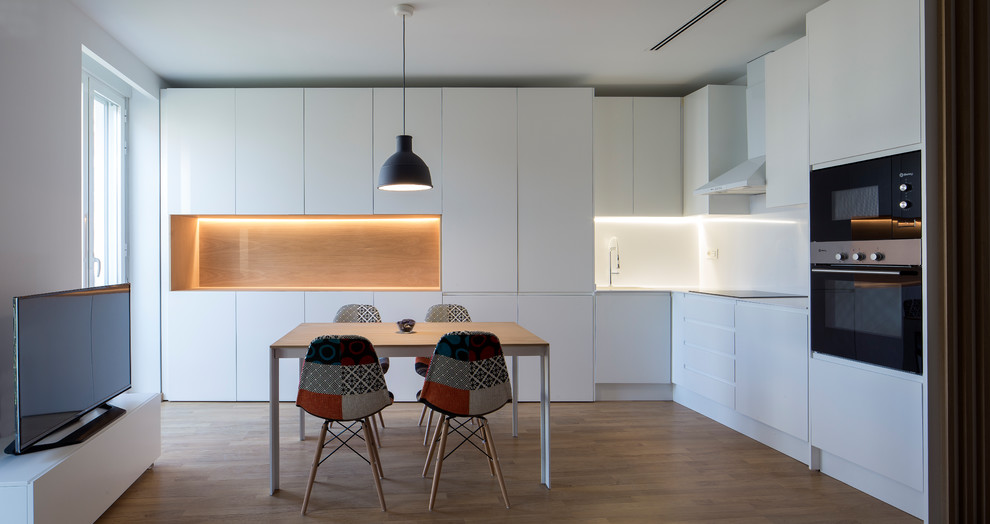 Medium sized scandi l-shaped kitchen/diner in Valencia with flat-panel cabinets, white cabinets, white splashback, black appliances, light hardwood flooring, no island and beige floors.