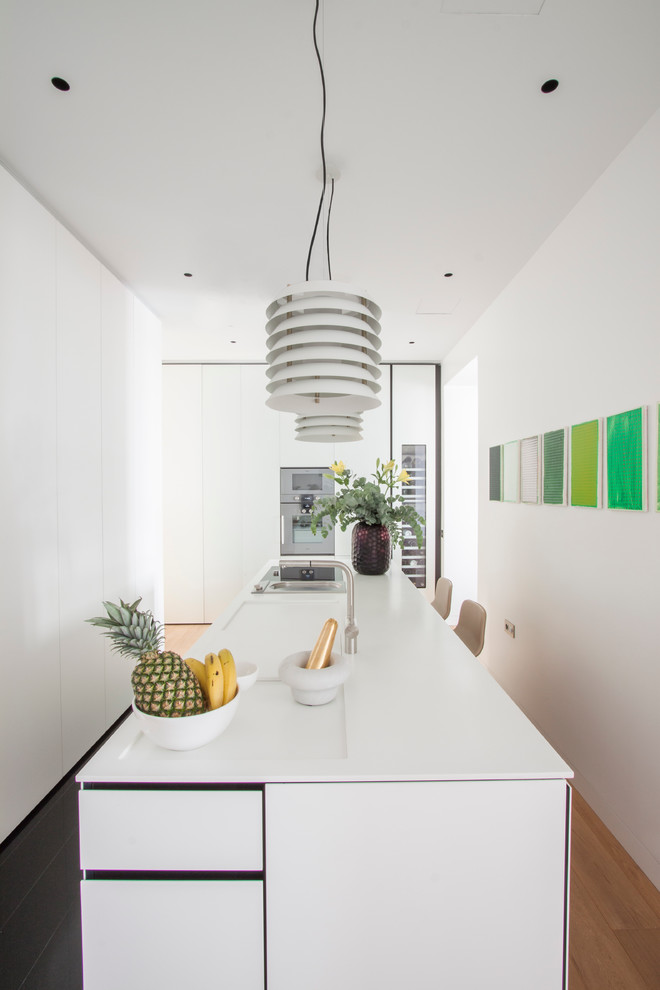 Example of a small danish l-shaped light wood floor enclosed kitchen design in Madrid with flat-panel cabinets, white cabinets, stainless steel appliances, an island and solid surface countertops
