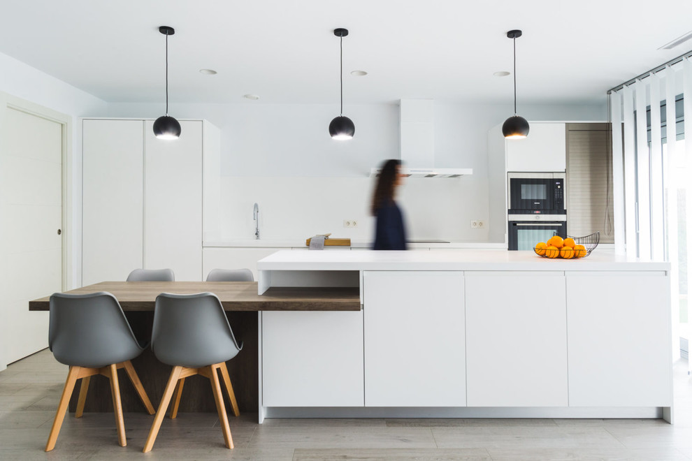 Einzeilige Nordische Küche mit weißen Schränken, Küchenrückwand in Weiß, Kücheninsel, weißer Arbeitsplatte, flächenbündigen Schrankfronten und hellem Holzboden in Barcelona