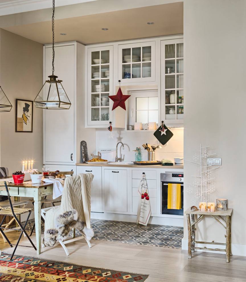 Small traditional single-wall kitchen/diner in Madrid with glass-front cabinets, white cabinets, white splashback, integrated appliances, light hardwood flooring, no island and wood worktops.