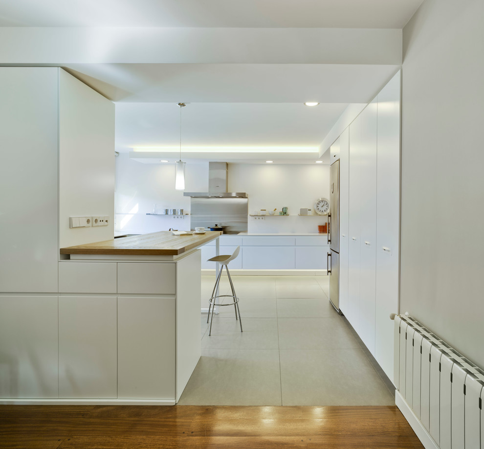Ejemplo de cocina actual grande con armarios con paneles lisos, puertas de armario blancas, electrodomésticos de acero inoxidable y península