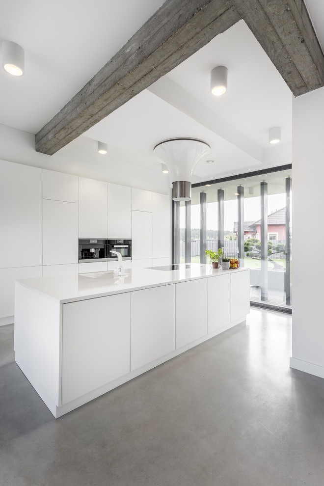 Ejemplo de cocina minimalista con armarios con paneles lisos, puertas de armario blancas, suelo de cemento, una isla, suelo gris y encimeras blancas