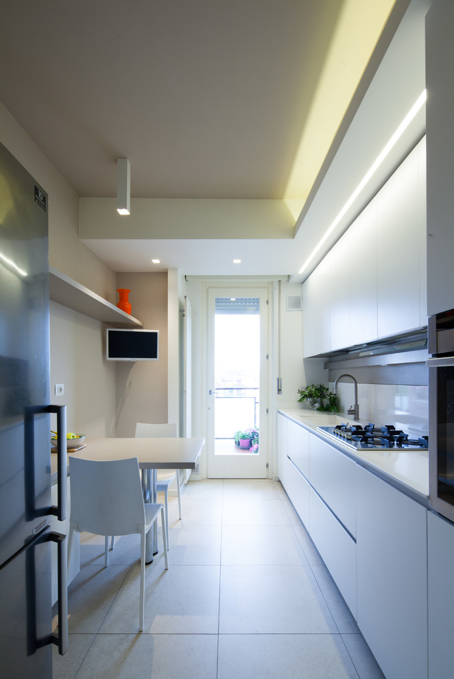 Modelo de cocina comedor minimalista pequeña con fregadero encastrado, armarios con paneles lisos, puertas de armario blancas, salpicadero blanco, electrodomésticos de acero inoxidable y suelo blanco