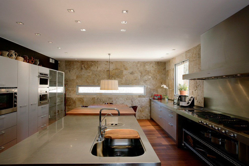 Example of a large trendy galley dark wood floor kitchen design in Barcelona with an integrated sink, flat-panel cabinets, gray cabinets, stainless steel countertops, metallic backsplash, metal backsplash, stainless steel appliances and an island
