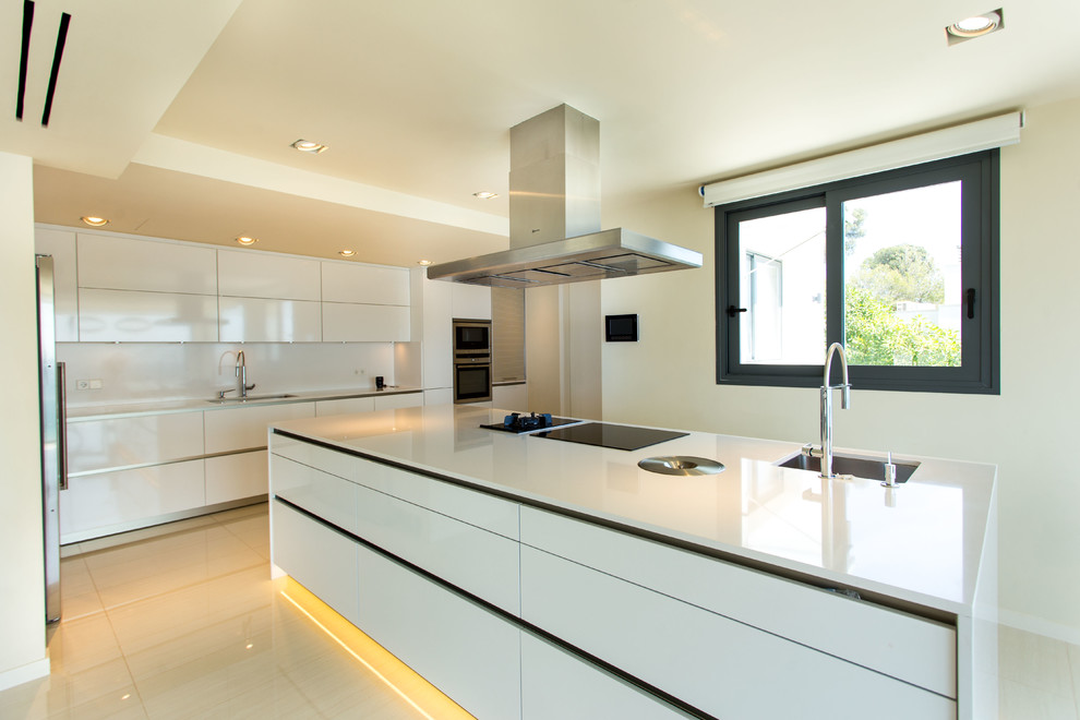 Modern inredning av ett stort linjärt kök med öppen planlösning, med en enkel diskho, släta luckor, vita skåp, vitt stänkskydd, rostfria vitvaror och en köksö