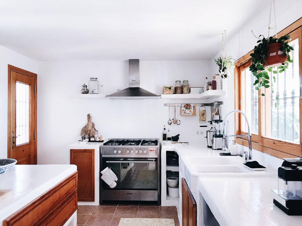 Medelhavsstil inredning av ett stort vit vitt kök, med en dubbel diskho, skåp i mellenmörkt trä, bänkskiva i betong, rostfria vitvaror, klinkergolv i terrakotta, en köksö och brunt golv