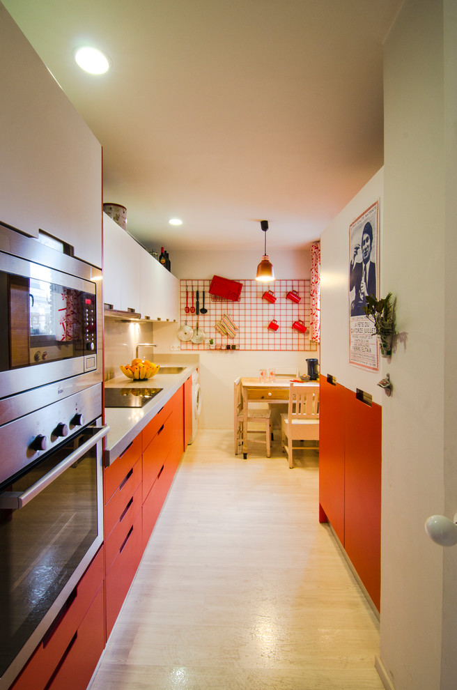 Cette photo montre une cuisine linéaire éclectique fermée et de taille moyenne avec un évier 1 bac, un placard à porte plane, des portes de placard rouges, un électroménager en acier inoxydable et aucun îlot.