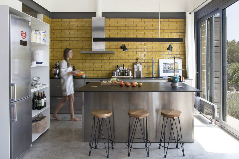 Exempel på ett industriellt kök, med en nedsänkt diskho, gult stänkskydd, rostfria vitvaror, betonggolv och en köksö
