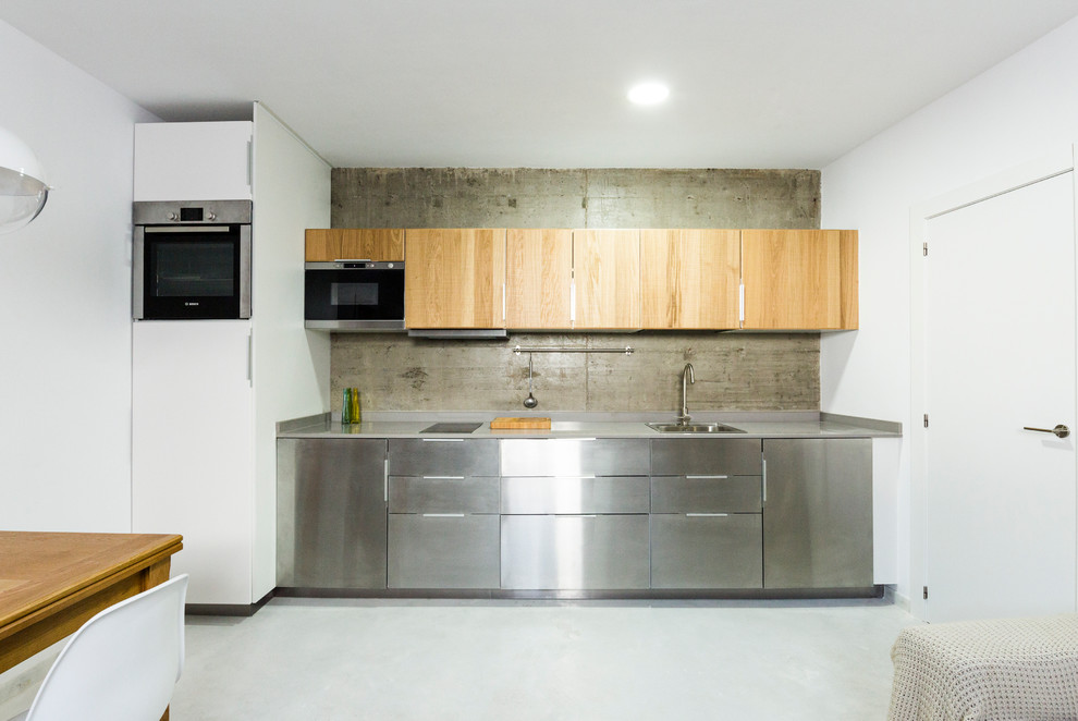 Immagine di una cucina nordica di medie dimensioni con lavello a vasca singola, ante lisce, ante in acciaio inossidabile, pavimento in cemento e nessuna isola