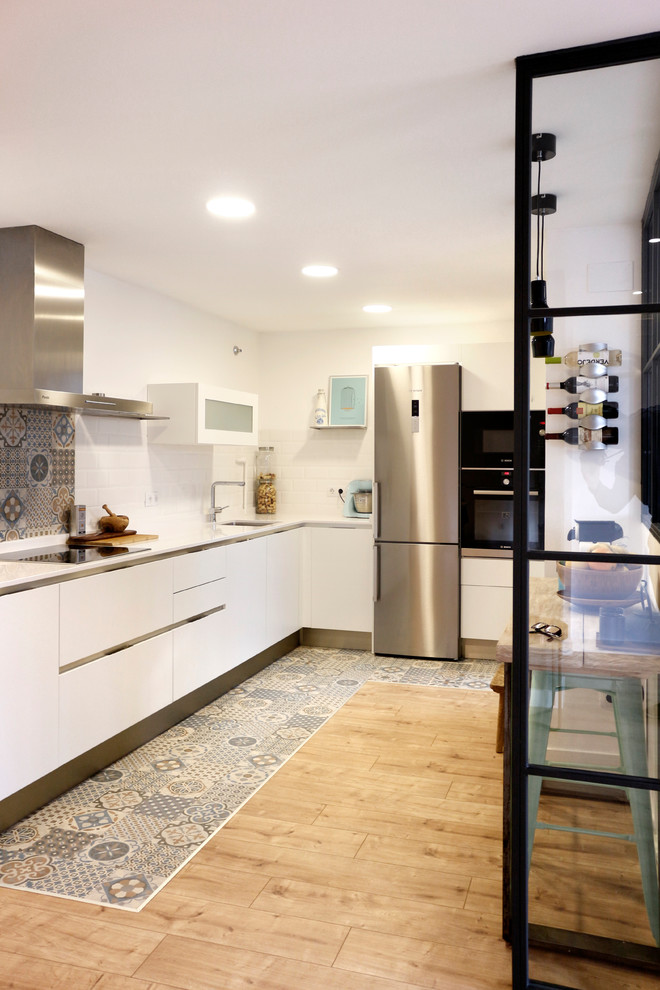Свежая идея для дизайна: угловая кухня-гостиная среднего размера в стиле лофт с одинарной мойкой, плоскими фасадами, белыми фасадами и техникой из нержавеющей стали без острова - отличное фото интерьера