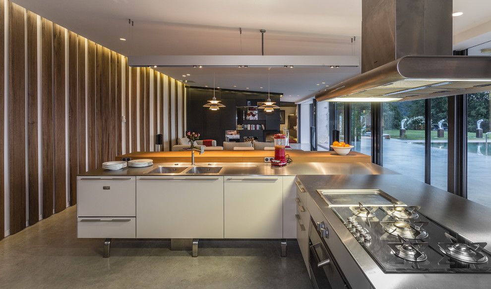 Photo of a large industrial l-shaped open plan kitchen in Barcelona with an integrated sink, flat-panel cabinets, white cabinets, stainless steel worktops, concrete flooring and no island.