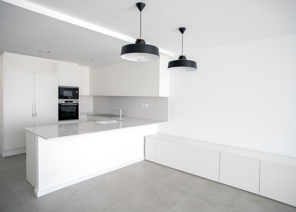 This is an example of a medium sized modern u-shaped open plan kitchen in Barcelona with a single-bowl sink, flat-panel cabinets, white cabinets, white splashback, stainless steel appliances, no island, grey floors and white worktops.