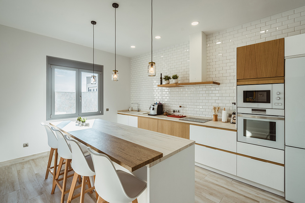 Bild på ett nordiskt beige linjärt beige kök, med släta luckor, träbänkskiva, vitt stänkskydd, stänkskydd i tunnelbanekakel, vita vitvaror, en köksö, en enkel diskho, vita skåp och beiget golv