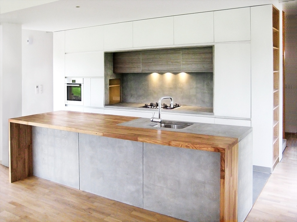 Medium sized contemporary single-wall open plan kitchen in Madrid with flat-panel cabinets, white cabinets, wood worktops, grey splashback and an island.