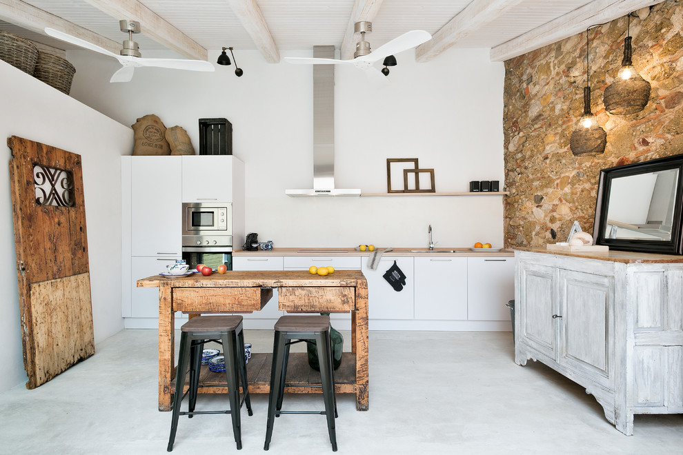 Immagine di una cucina stile rurale di medie dimensioni con lavello a vasca singola, ante lisce, ante bianche, top in legno, paraspruzzi bianco, elettrodomestici in acciaio inossidabile e pavimento in cemento