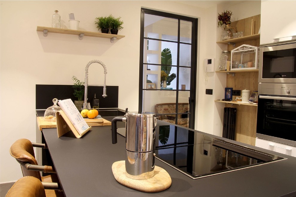 Example of a mid-sized trendy single-wall gray floor enclosed kitchen design in Bilbao with a single-bowl sink, black cabinets, stainless steel appliances, an island and black countertops
