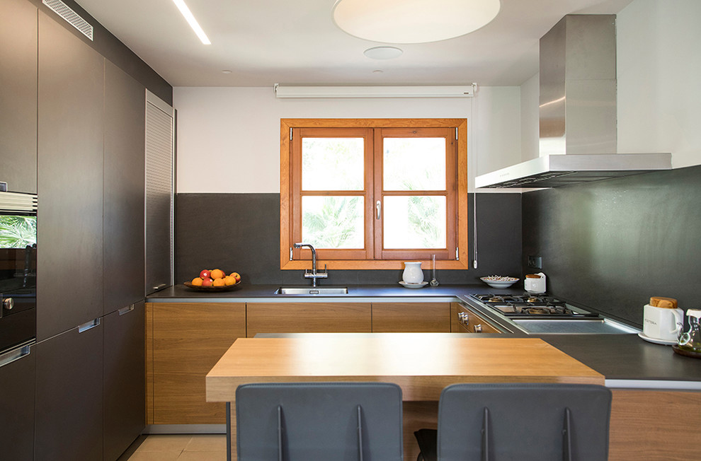 Exemple d'une petite cuisine ouverte tendance en bois brun et U avec un placard à porte plane, une crédence noire, un électroménager en acier inoxydable, un sol beige et une péninsule.