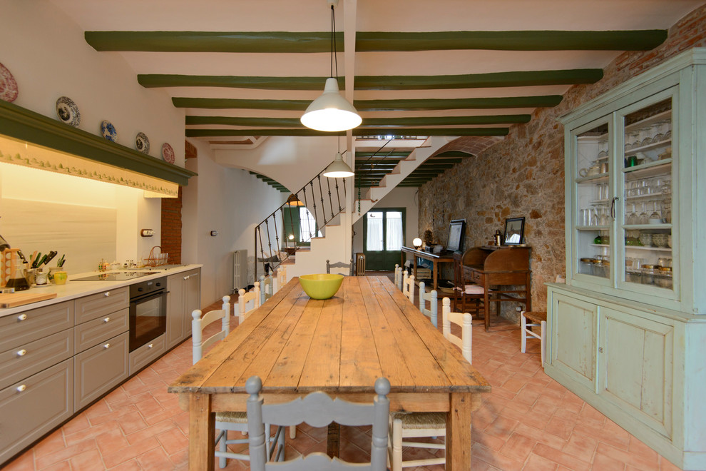 バルセロナにある広い地中海スタイルのおしゃれなキッチン (ベージュのキャビネット、テラコッタタイルの床、アイランドなし、赤い床、白いキッチンパネル、落し込みパネル扉のキャビネット、黒い調理設備) の写真