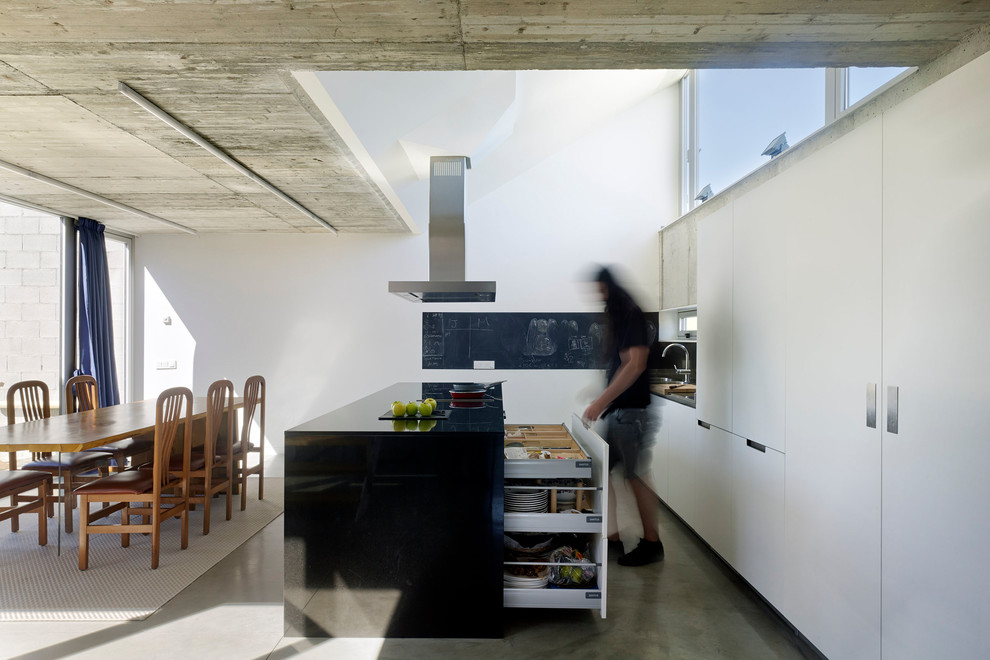 Photo of a medium sized contemporary kitchen/diner in Other with flat-panel cabinets, white cabinets, granite worktops, concrete flooring, an island, grey floors and black worktops.