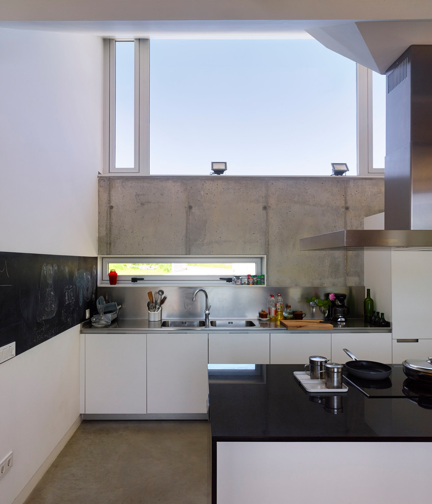 Idéer för mellanstora funkis kök med öppen planlösning, med en dubbel diskho, släta luckor, vita skåp, granitbänkskiva, stänkskydd med metallisk yta, stänkskydd i metallkakel, rostfria vitvaror, betonggolv, en köksö och grått golv