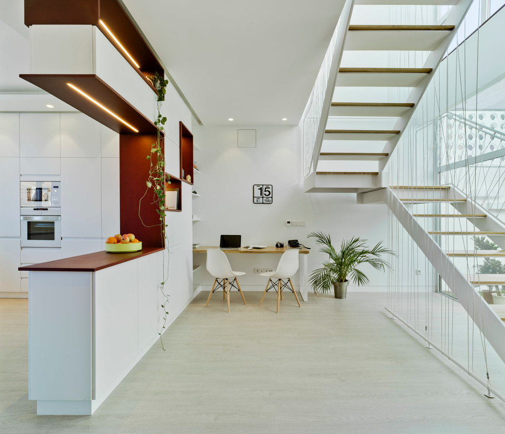 Example of a mid-sized trendy single-wall light wood floor open concept kitchen design in Other with flat-panel cabinets, white cabinets, white appliances and a peninsula