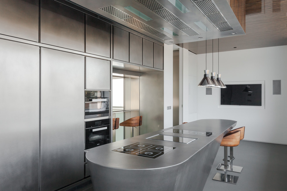 Large contemporary galley enclosed kitchen in Madrid with flat-panel cabinets, stainless steel cabinets, stainless steel worktops, stainless steel appliances, concrete flooring and an island.