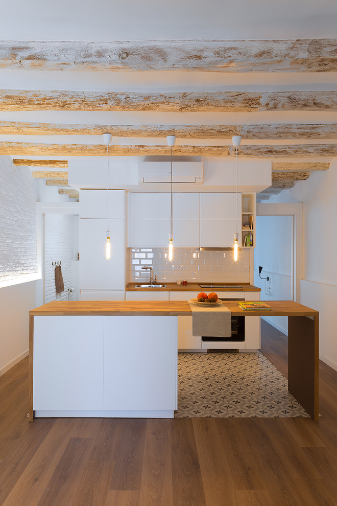Inspiration for a small contemporary single-wall open plan kitchen in Barcelona with a single-bowl sink, flat-panel cabinets, white cabinets, wood worktops, white splashback, metro tiled splashback, integrated appliances, cement flooring, an island and white floors.