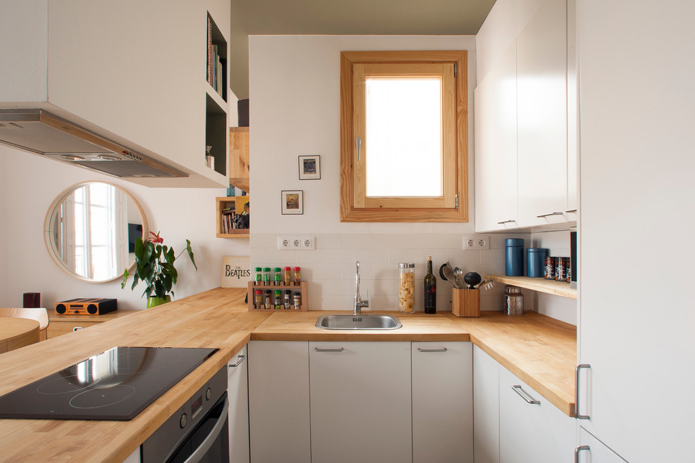 Small scandi u-shaped open plan kitchen in Barcelona with a single-bowl sink, flat-panel cabinets, white cabinets, wood worktops, white splashback, stainless steel appliances and no island.