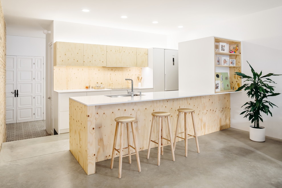 Foto på ett minimalistiskt vit kök, med en undermonterad diskho, släta luckor, skåp i ljust trä, stänkskydd i trä, betonggolv, en halv köksö och grått golv
