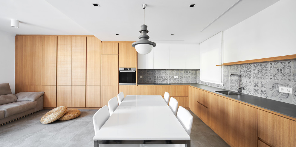 Offene Moderne Küche in L-Form mit flächenbündigen Schrankfronten, hellbraunen Holzschränken, Küchenrückwand in Grau, grauem Boden, grauer Arbeitsplatte und Unterbauwaschbecken in Sonstige