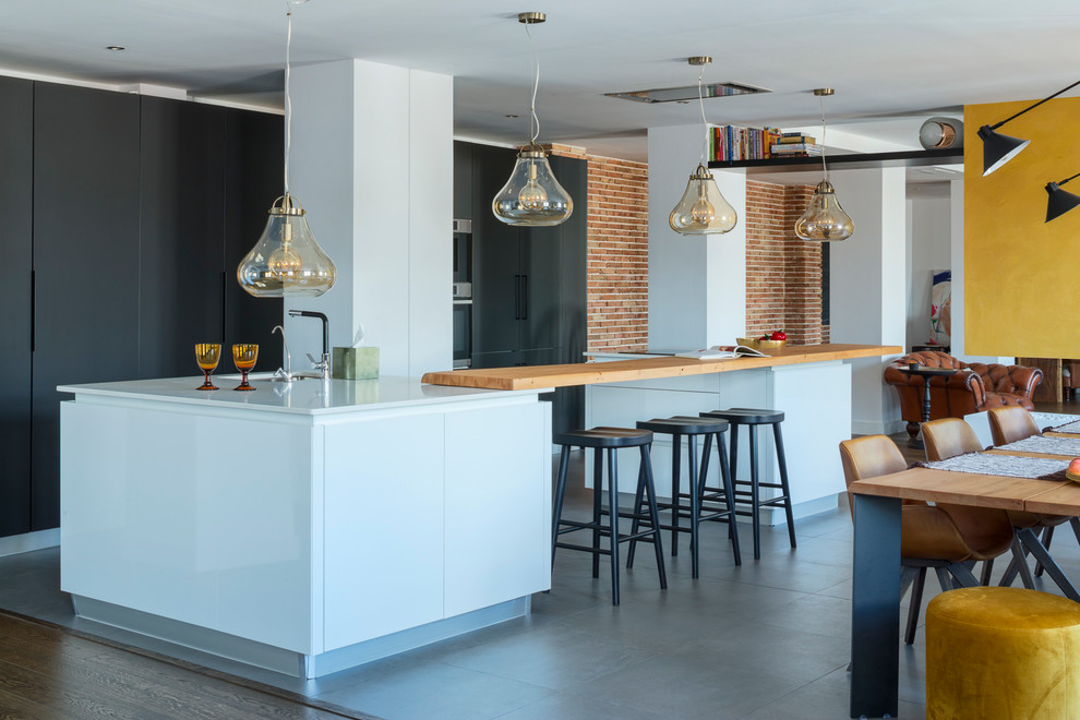 Large contemporary u-shaped open plan kitchen in Malaga with flat-panel cabinets, black cabinets, engineered stone countertops, integrated appliances, ceramic flooring, multiple islands, grey floors, white worktops and a submerged sink.