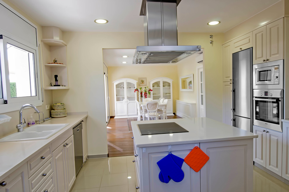 Inredning av ett klassiskt avskilt, mellanstort l-kök, med en dubbel diskho, luckor med infälld panel, vita skåp, rostfria vitvaror och en köksö