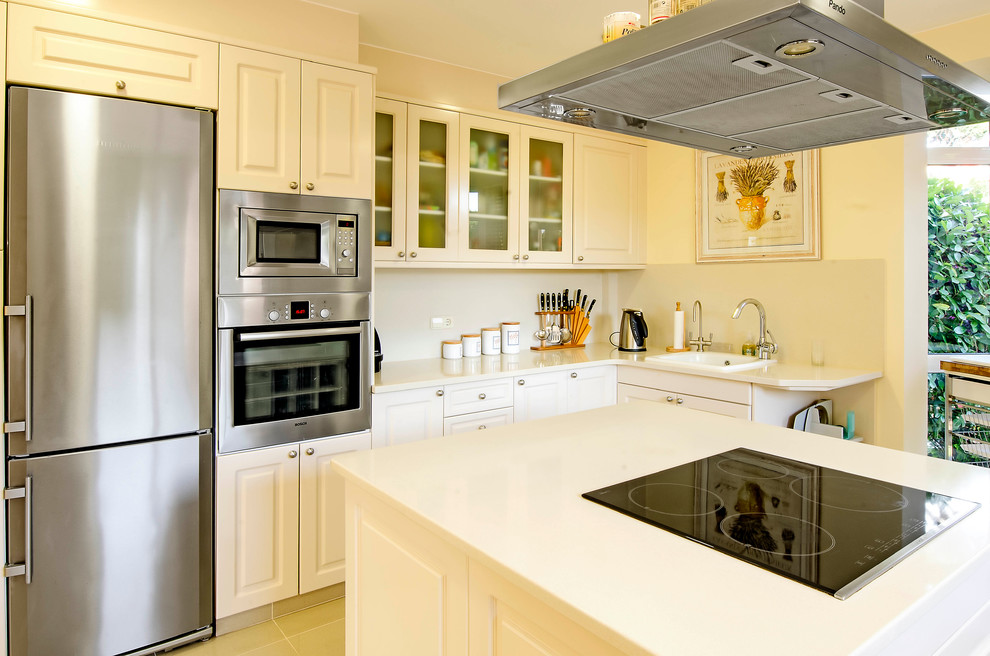 This is an example of a medium sized traditional u-shaped enclosed kitchen in Other with a built-in sink, raised-panel cabinets, white cabinets, engineered stone countertops, beige splashback, stainless steel appliances, ceramic flooring and an island.