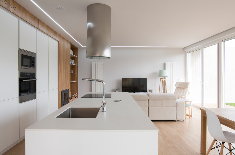 Foto på ett funkis vit kök, med släta luckor, vita skåp, rostfria vitvaror, en köksö, en undermonterad diskho, ljust trägolv och beiget golv