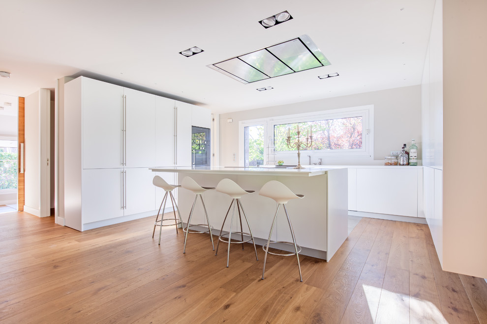Medium sized contemporary u-shaped enclosed kitchen in Madrid with flat-panel cabinets, white cabinets, medium hardwood flooring and an island.